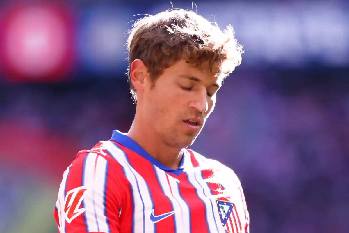 Jugador de fútbol con uniforme del Atlético de Madrid con los ojos cerrados en el campo.