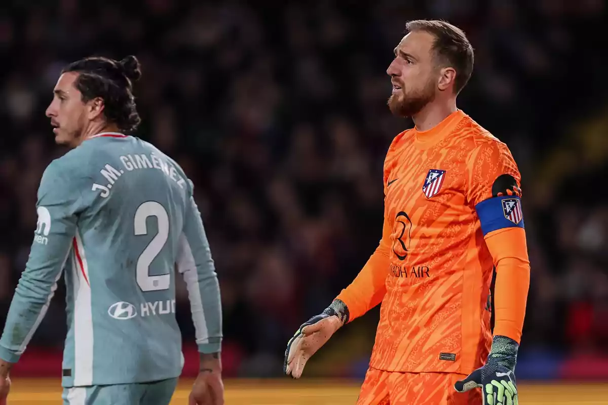 Dos jugadores de fútbol en el campo, uno con uniforme gris y el otro con uniforme naranja, ambos del Atlético de Madrid.