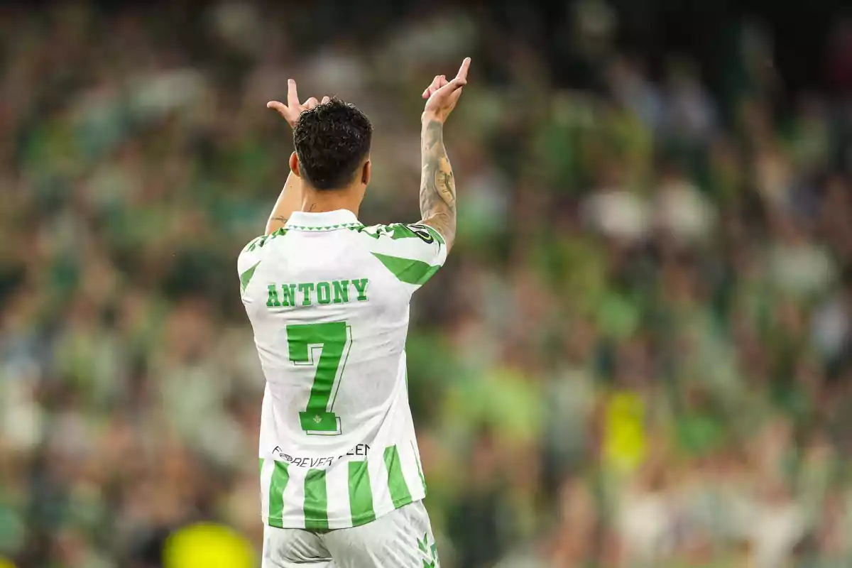 Un jugador de fútbol con el número 7 en su camiseta levanta las manos en un estadio lleno de espectadores. Un jugador de fútbol con el número 7 en su camiseta levanta las manos en un estadio lleno de espectadores.