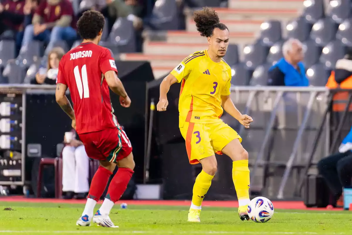 Dos futbolistas disputan el balón durante un partido uno con uniforme amarillo y el otro con uniforme rojo Dos futbolistas disputan el balón durante un partido uno con uniforme amarillo y el otro con uniforme rojo
