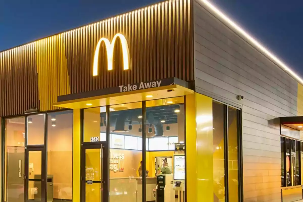 Fachada de un restaurante de comida rápida con un gran logotipo amarillo iluminado en la parte superior.