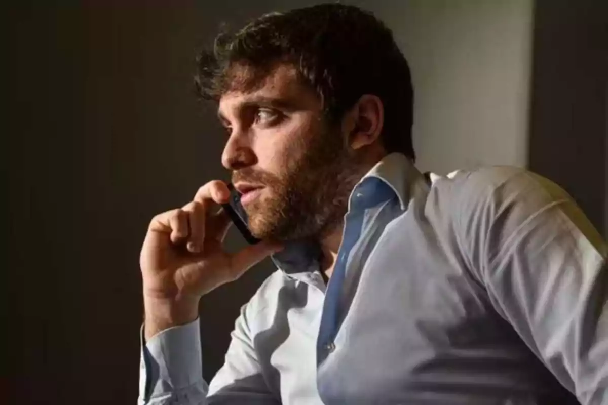 Hombre con barba hablando por teléfono móvil mientras lleva una camisa azul claro.
