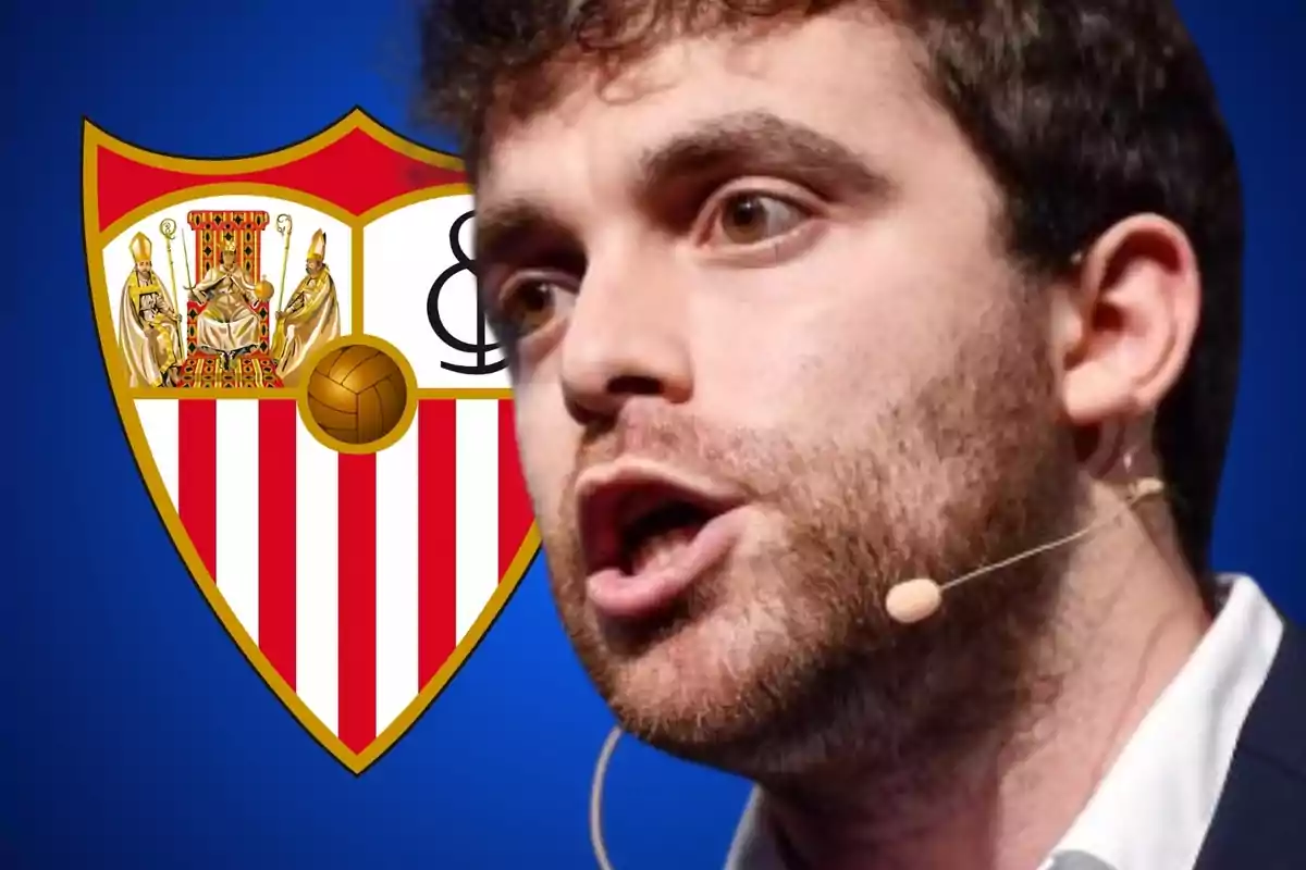 Hombre hablando con un micrófono de diadema frente al escudo del Sevilla FC.