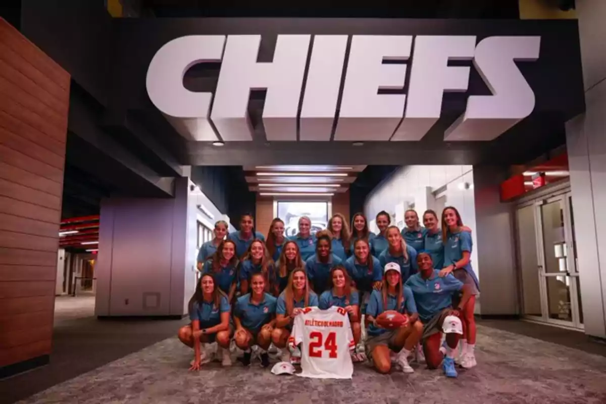 Un grupo de mujeres posando con una camiseta y un balón de fútbol americano bajo un letrero que dice "CHIEFS".