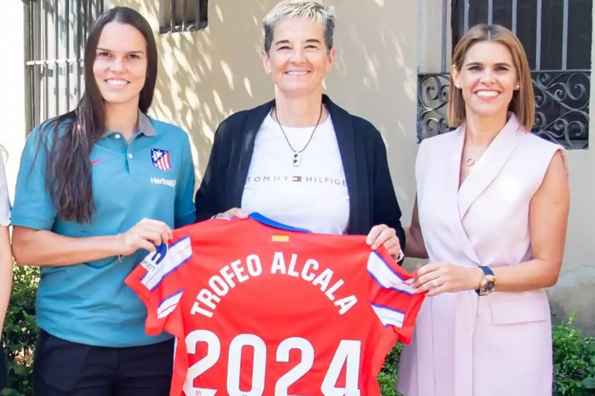 Tres mujeres sonrientes posan con una camiseta roja que dice "TROFEO ALCALA 2024".