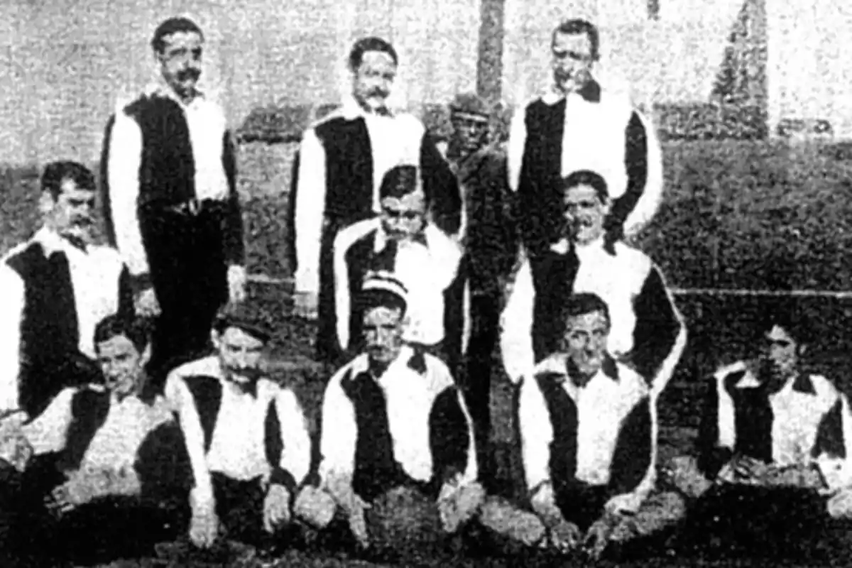 Un equipo de fútbol antiguo posando para una foto en blanco y negro, con los jugadores vistiendo uniformes de manga larga con colores oscuros y claros.