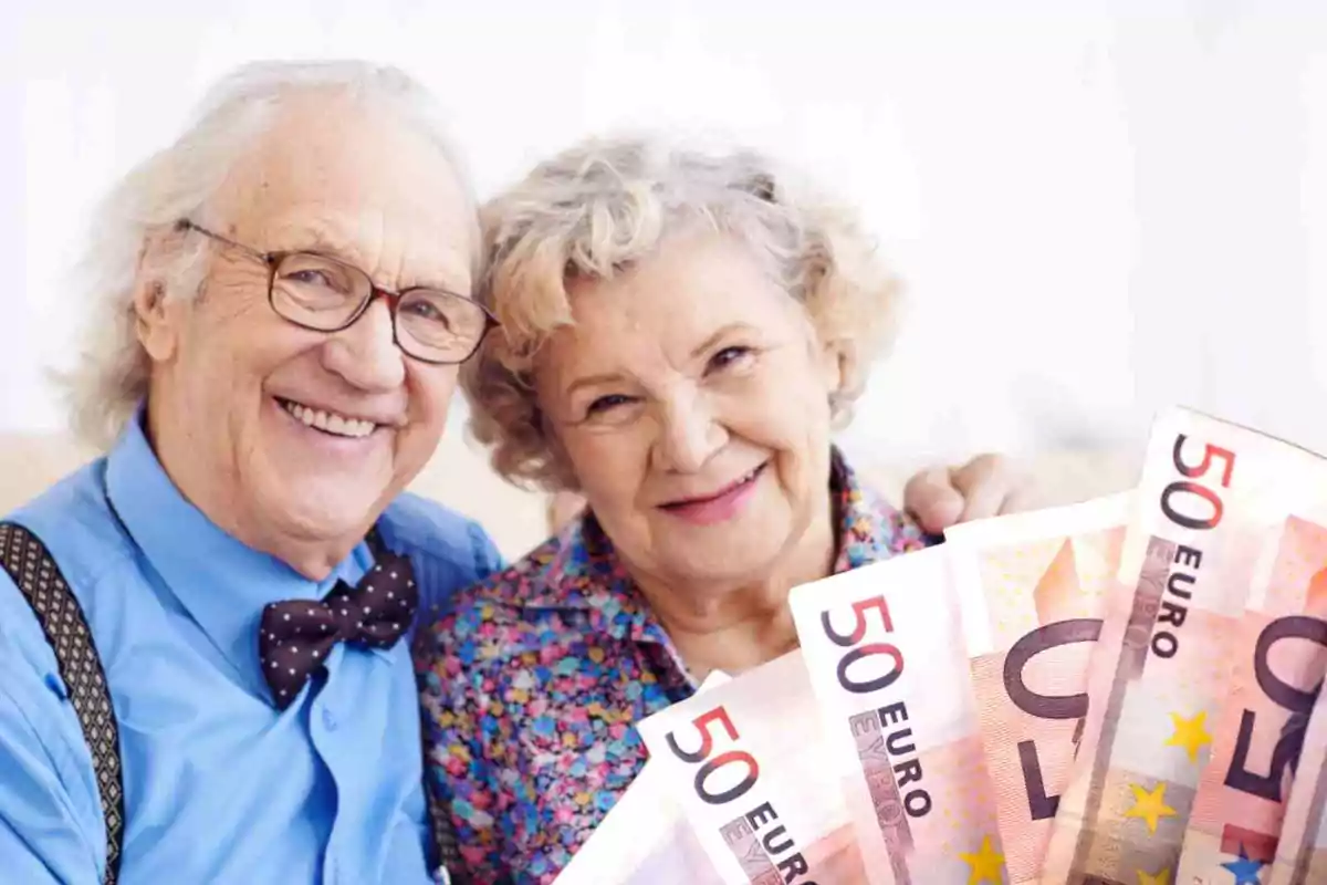 Una pareja de ancianos sonrientes sosteniendo billetes de 50 euros.