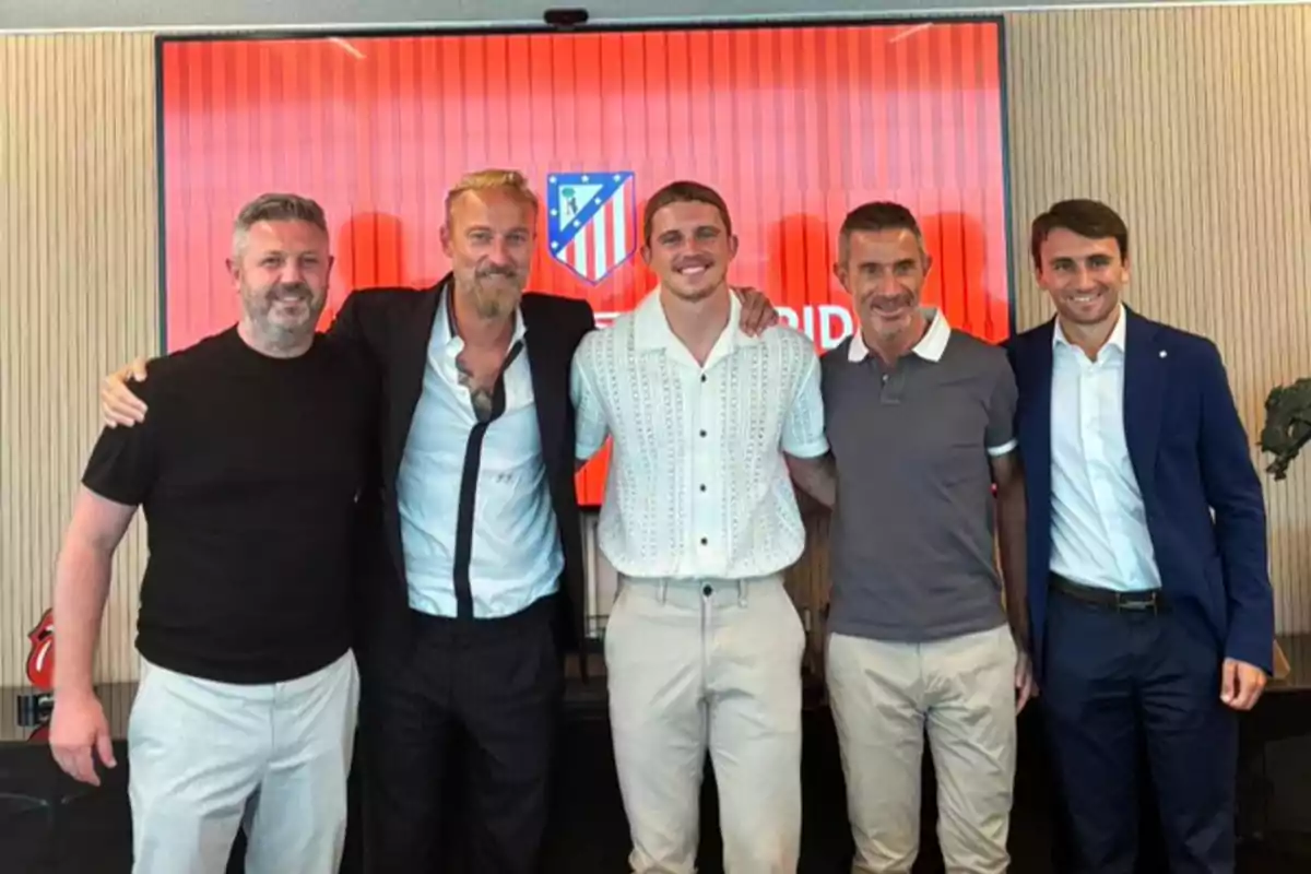 Cinco hombres posando juntos frente a un fondo con el logo del Atlético de Madrid.