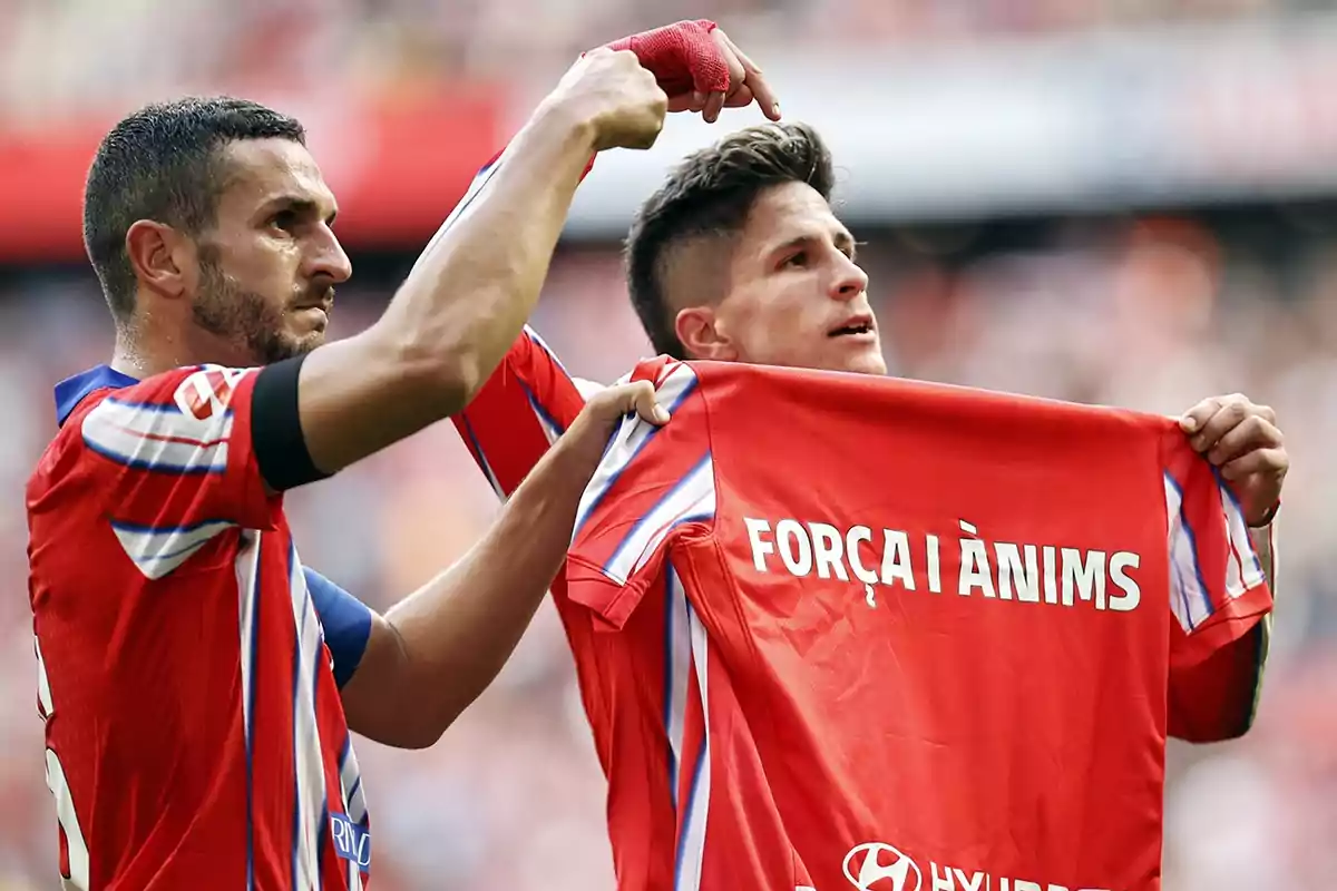 Dos jugadores de fútbol con camisetas rojas muestran un mensaje de apoyo en una camiseta.