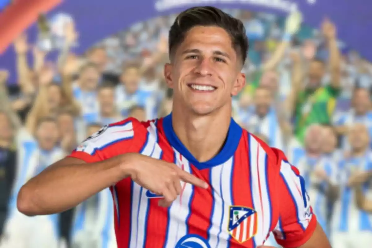 Jugador de fútbol sonriendo y señalando el escudo de su camiseta del Atlético de Madrid.