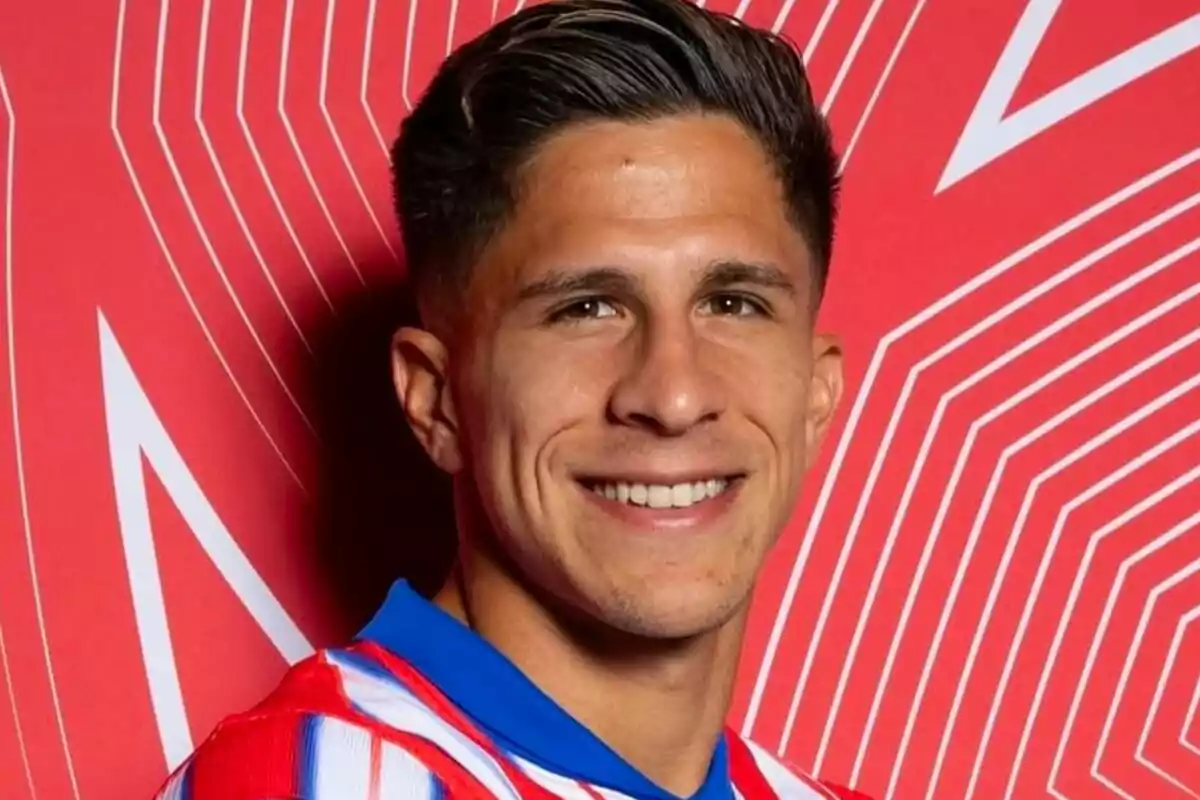 A man smiling in a red and white striped jersey in front of a red background with geometric patterns.