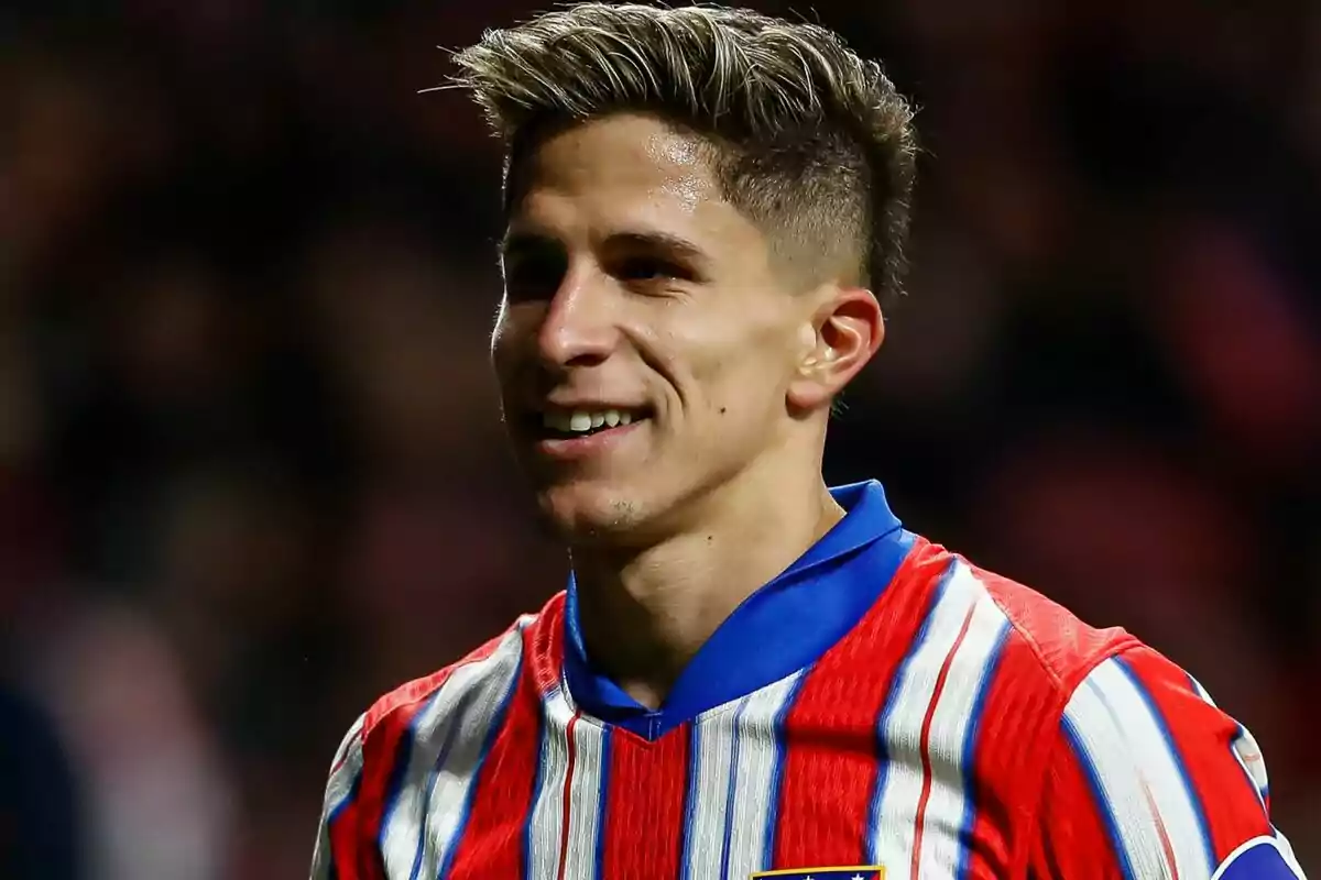 Un jugador de fútbol sonriendo con una camiseta de rayas rojas y blancas.