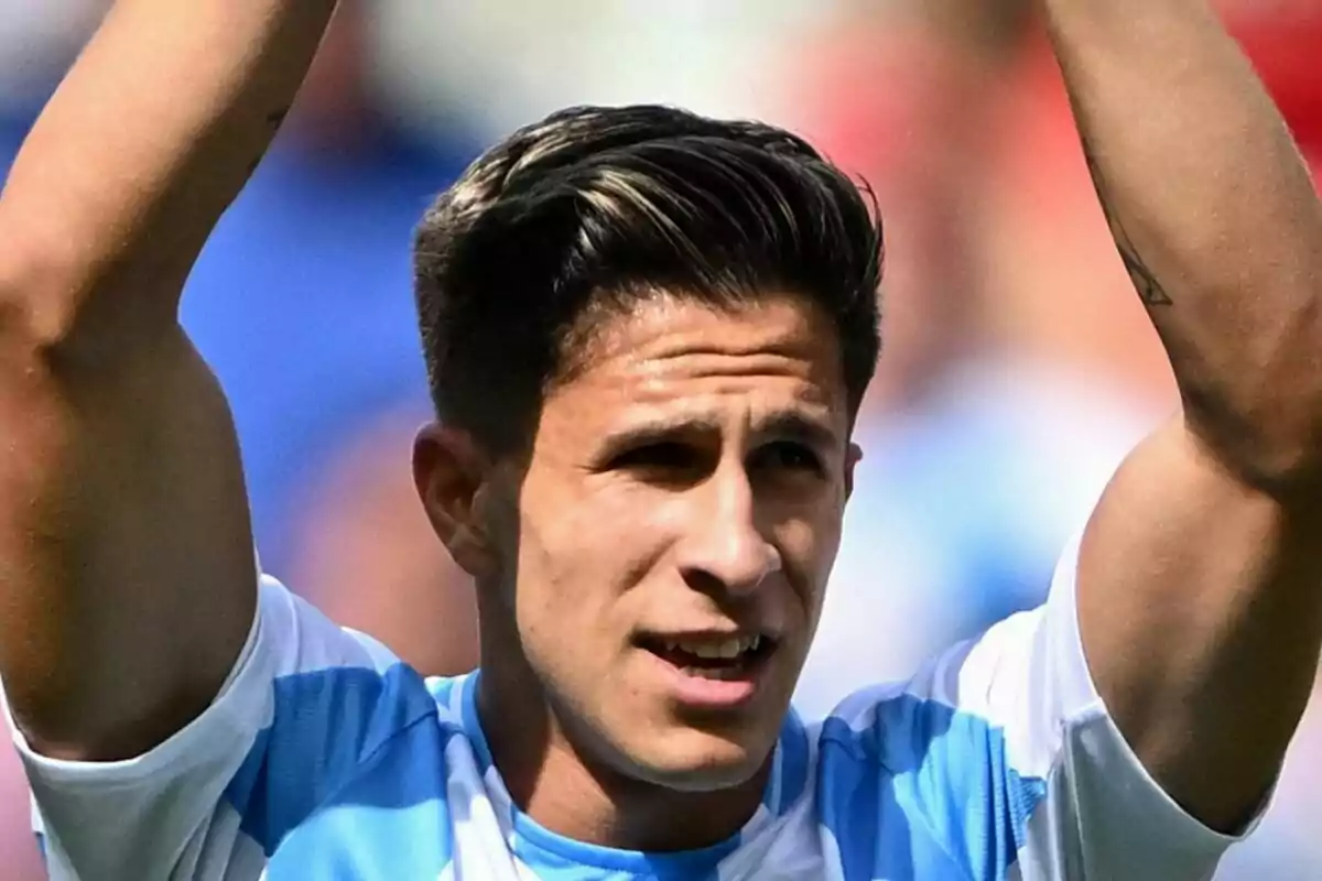 Un jugador de fútbol con uniforme celeste y blanco levanta los brazos en señal de celebración.