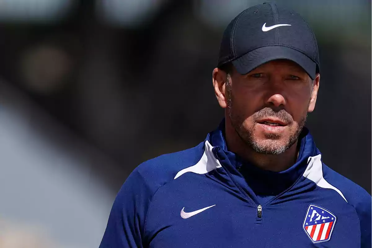 Hombre con gorra y chaqueta deportiva azul con logotipo de Nike y escudo de equipo.