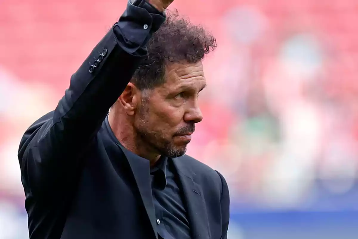 Hombre con traje negro levantando el brazo en un estadio.