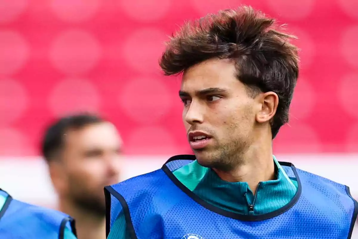 Un jugador de fútbol con chaleco de entrenamiento azul en un campo con fondo desenfocado.