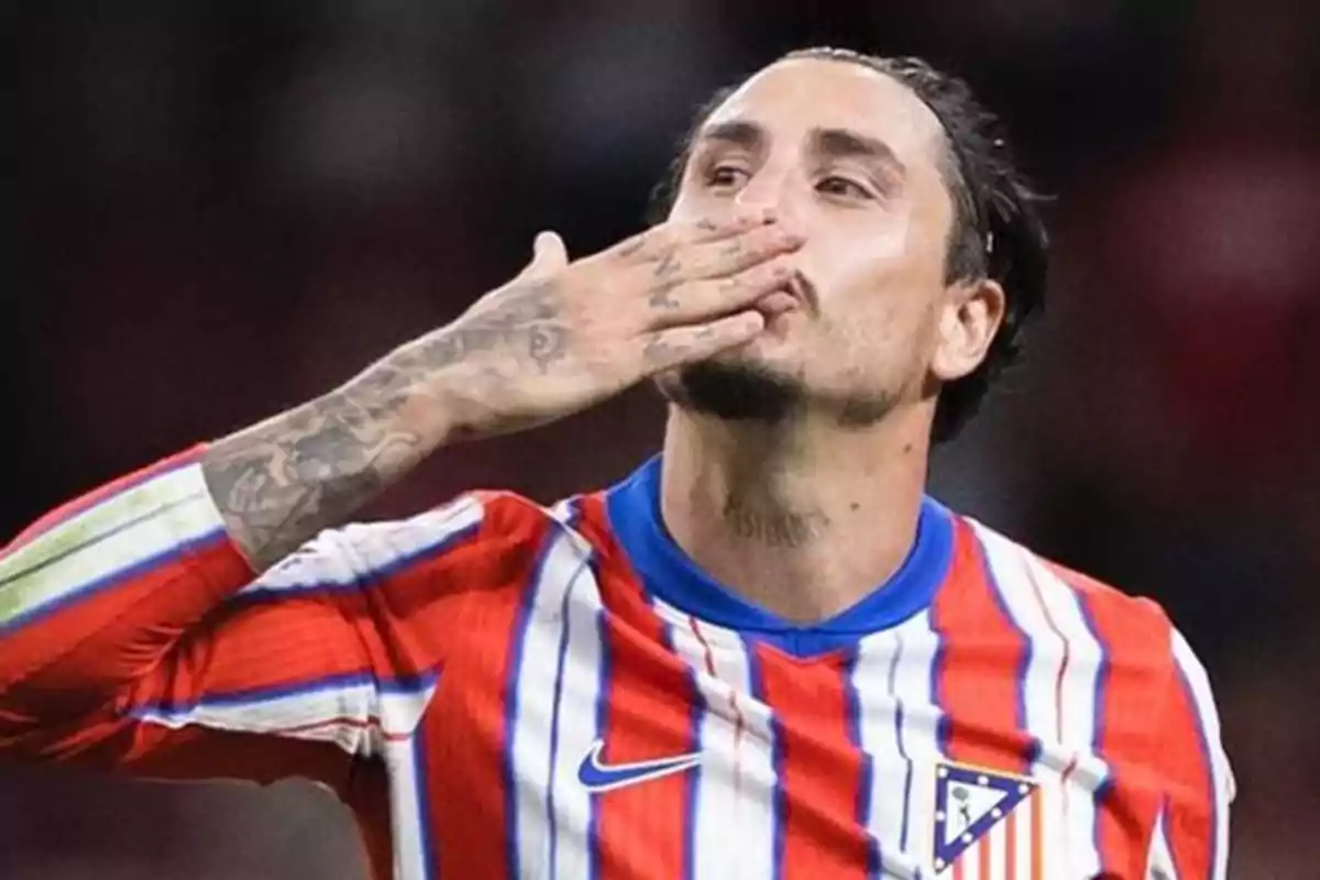 Jugador de fútbol con uniforme a rayas rojas, blancas y azules, enviando un beso con la mano.