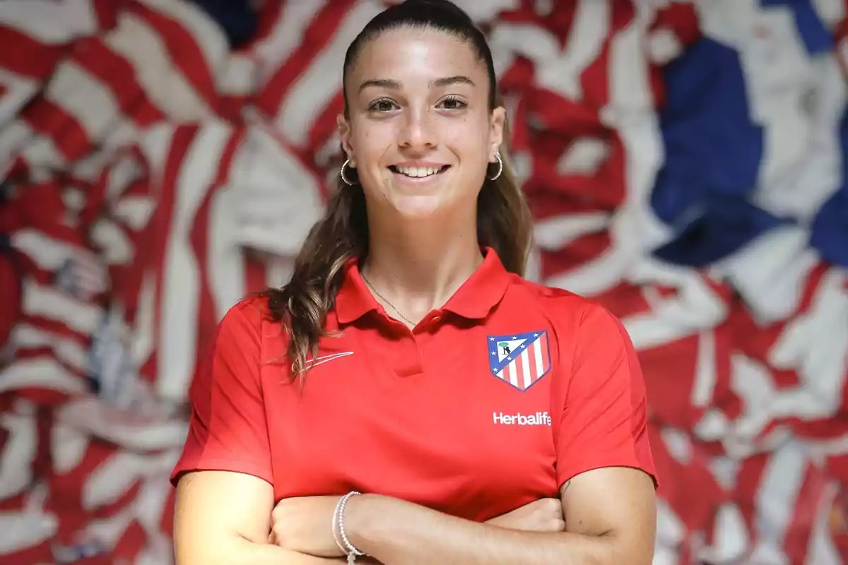 Mujer con camiseta roja del Atlético de Madrid sonriendo frente a un fondo de banderas del equipo.