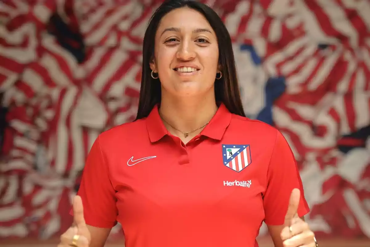 Persona con camiseta roja del Atlético de Madrid sonriendo y levantando ambos pulgares, con un fondo de colores rojo, blanco y azul.