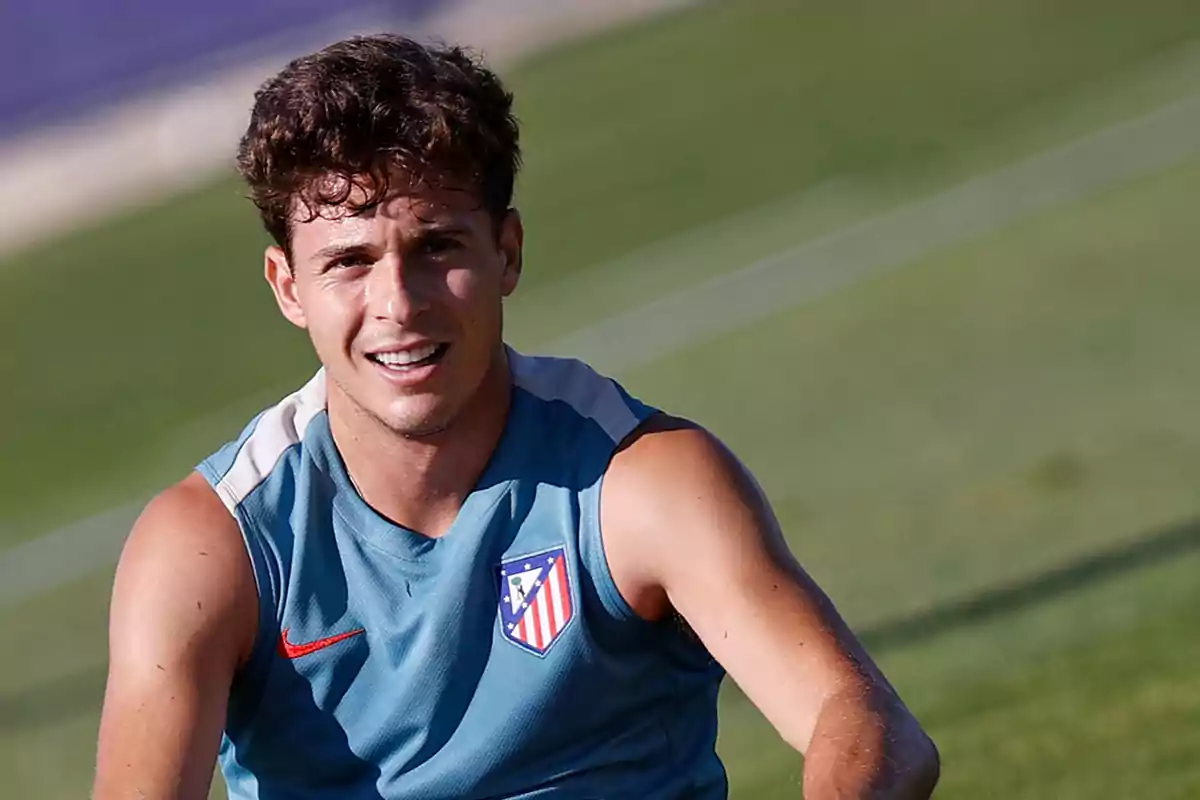 Un jugador de fútbol con una camiseta de entrenamiento del Atlético de Madrid sonríe mientras está en el campo.