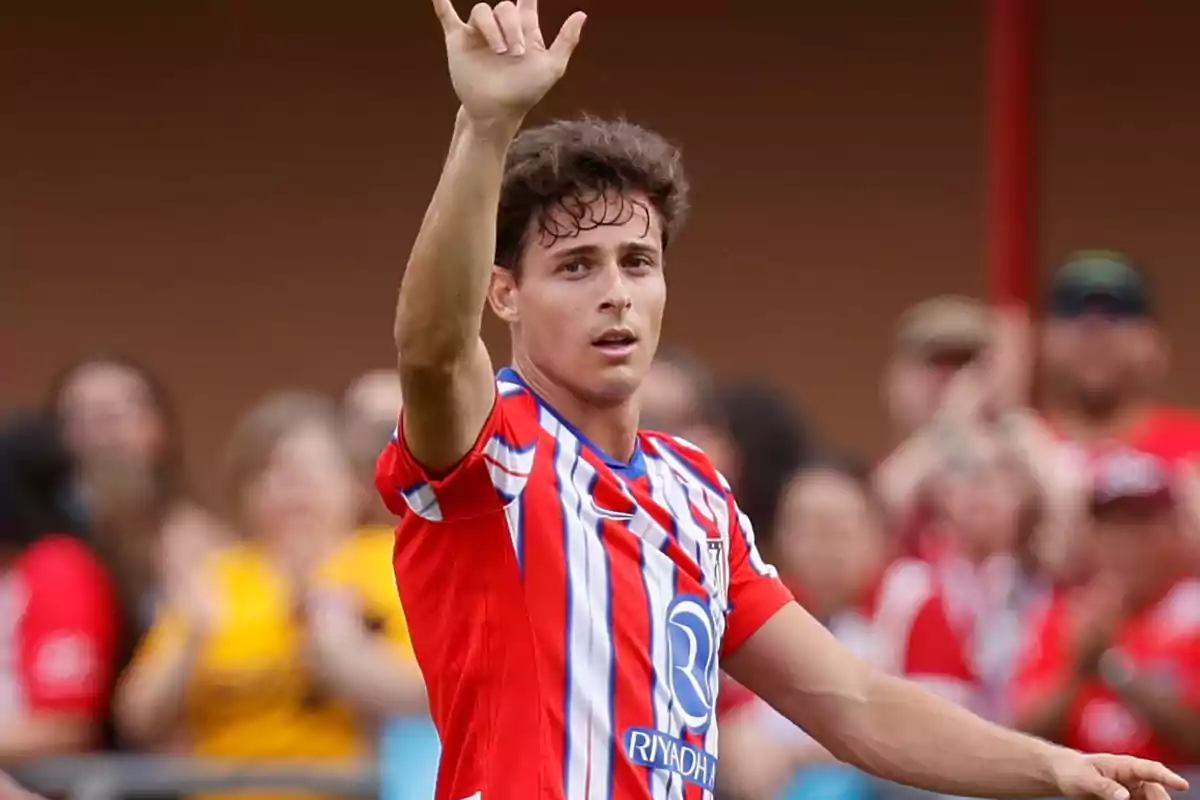 Un jugador de fútbol con uniforme rojo y blanco levantando la mano en señal de saludo durante un partido.