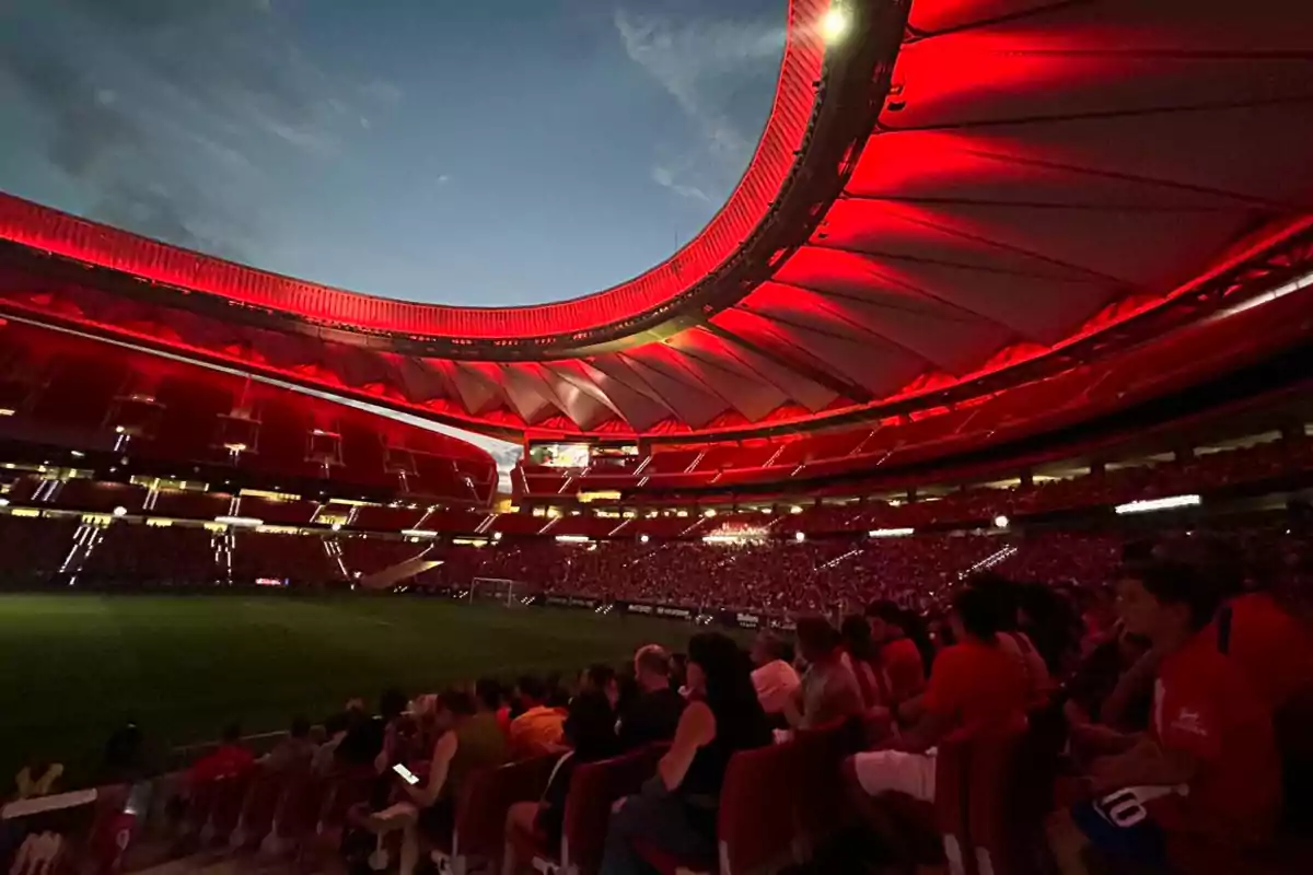 Estadio iluminado con luces rojas durante un evento nocturno, con espectadores en las gradas.