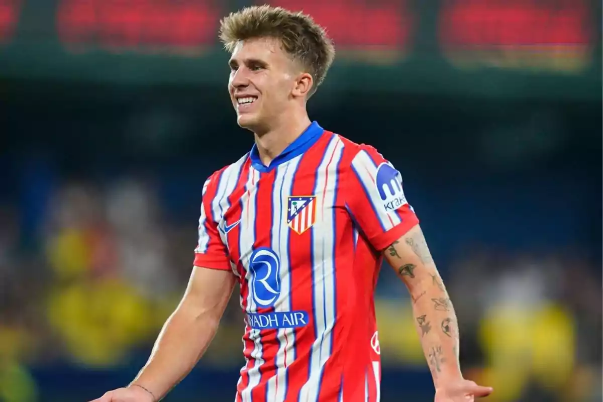 Jugador de fútbol con uniforme del Atlético de Madrid sonriendo en el campo.