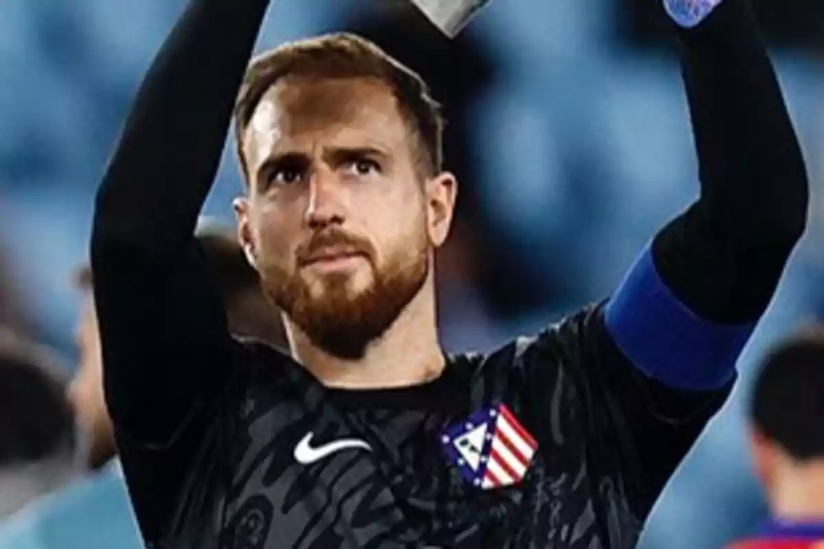 Un jugador de fútbol con uniforme negro y brazalete azul levanta los brazos en señal de celebración.