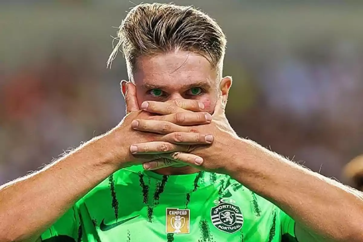 Un jugador de fútbol con uniforme verde se cubre la boca con las manos en un estadio.