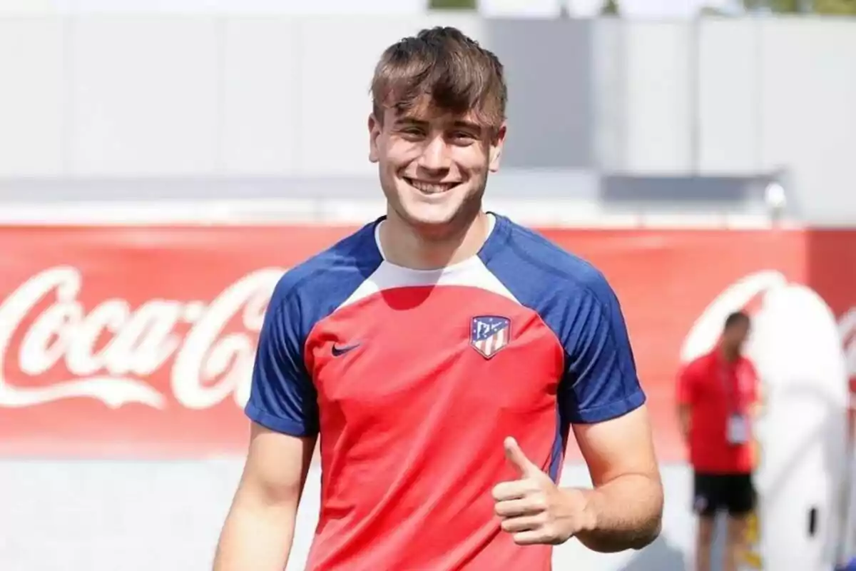 Un jugador de fútbol sonríe y hace un gesto de aprobación con el pulgar mientras viste una camiseta del Atlético de Madrid.