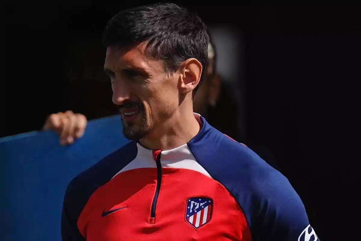 Hombre con barba y bigote, vistiendo una sudadera roja y azul con el escudo del Atlético de Madrid.