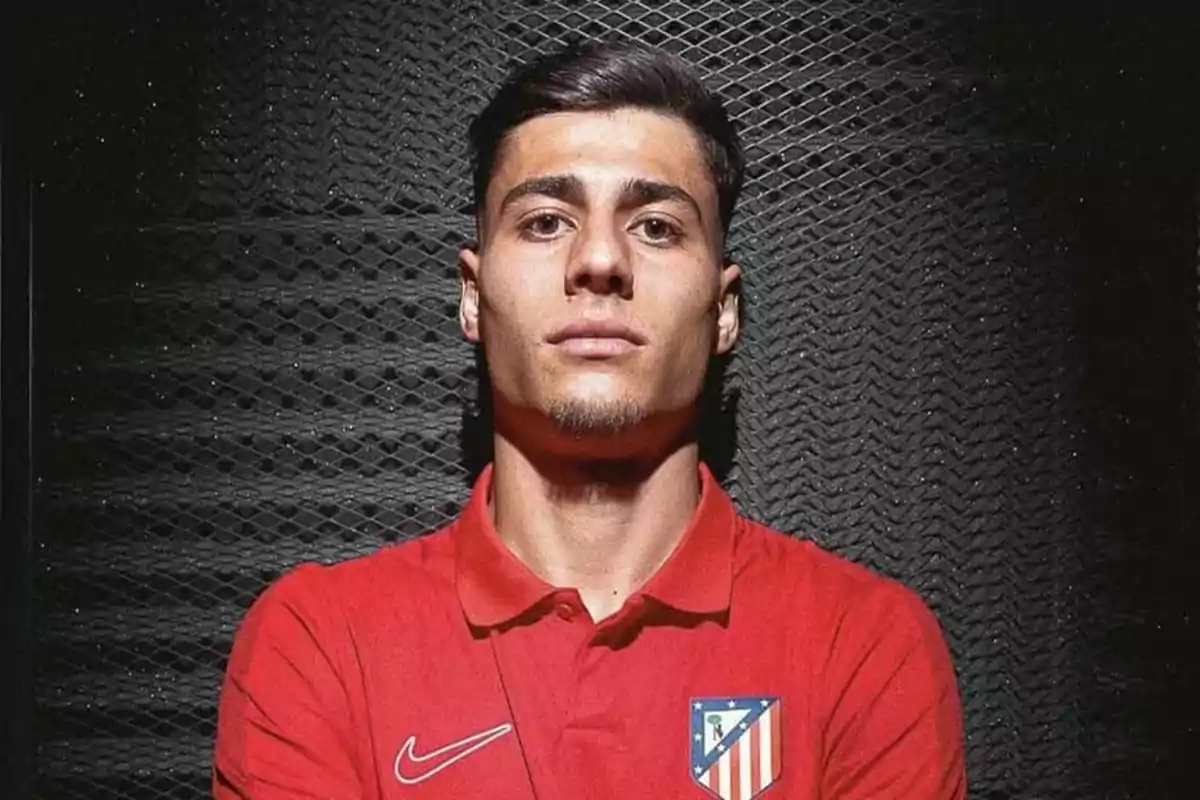 Un hombre con camiseta roja del Atlético de Madrid posando frente a un fondo oscuro.