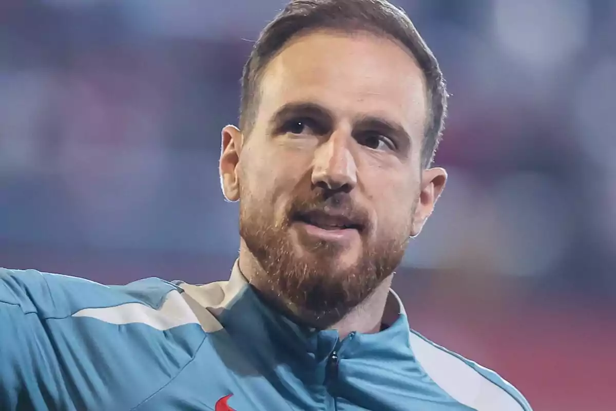 Un hombre con barba y chaqueta deportiva azul en un entorno desenfocado.