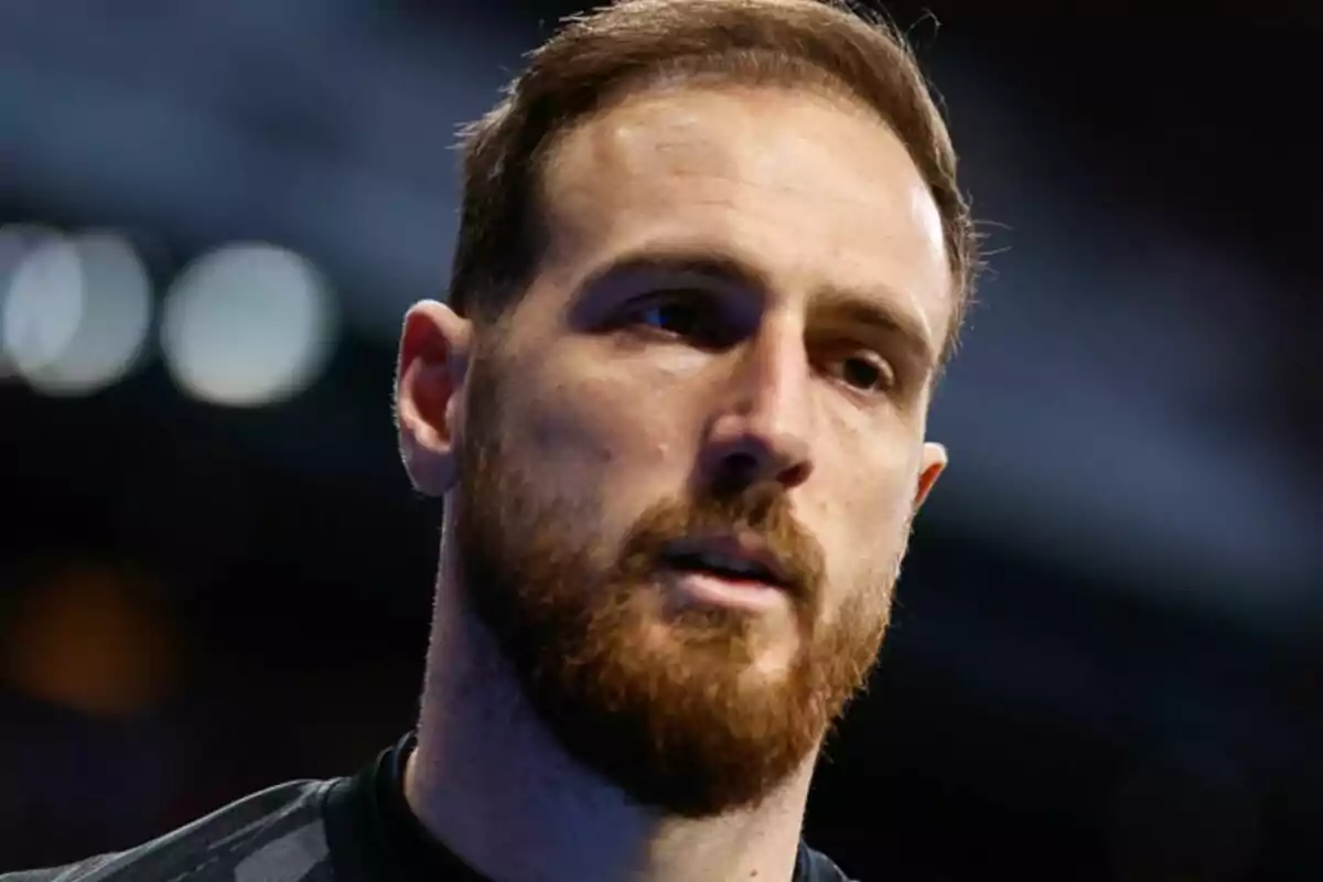 Un hombre con barba y cabello corto en un entorno oscuro.
