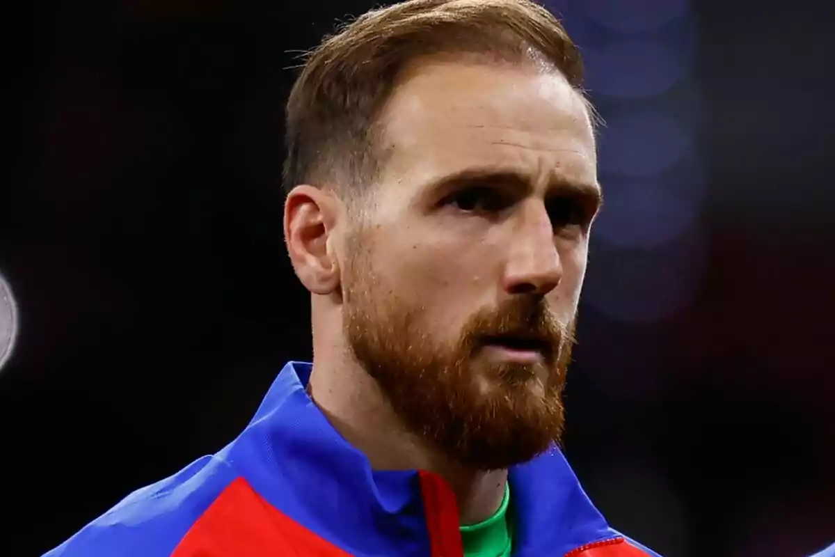 Un hombre con barba y cabello corto lleva una chaqueta azul y roja.