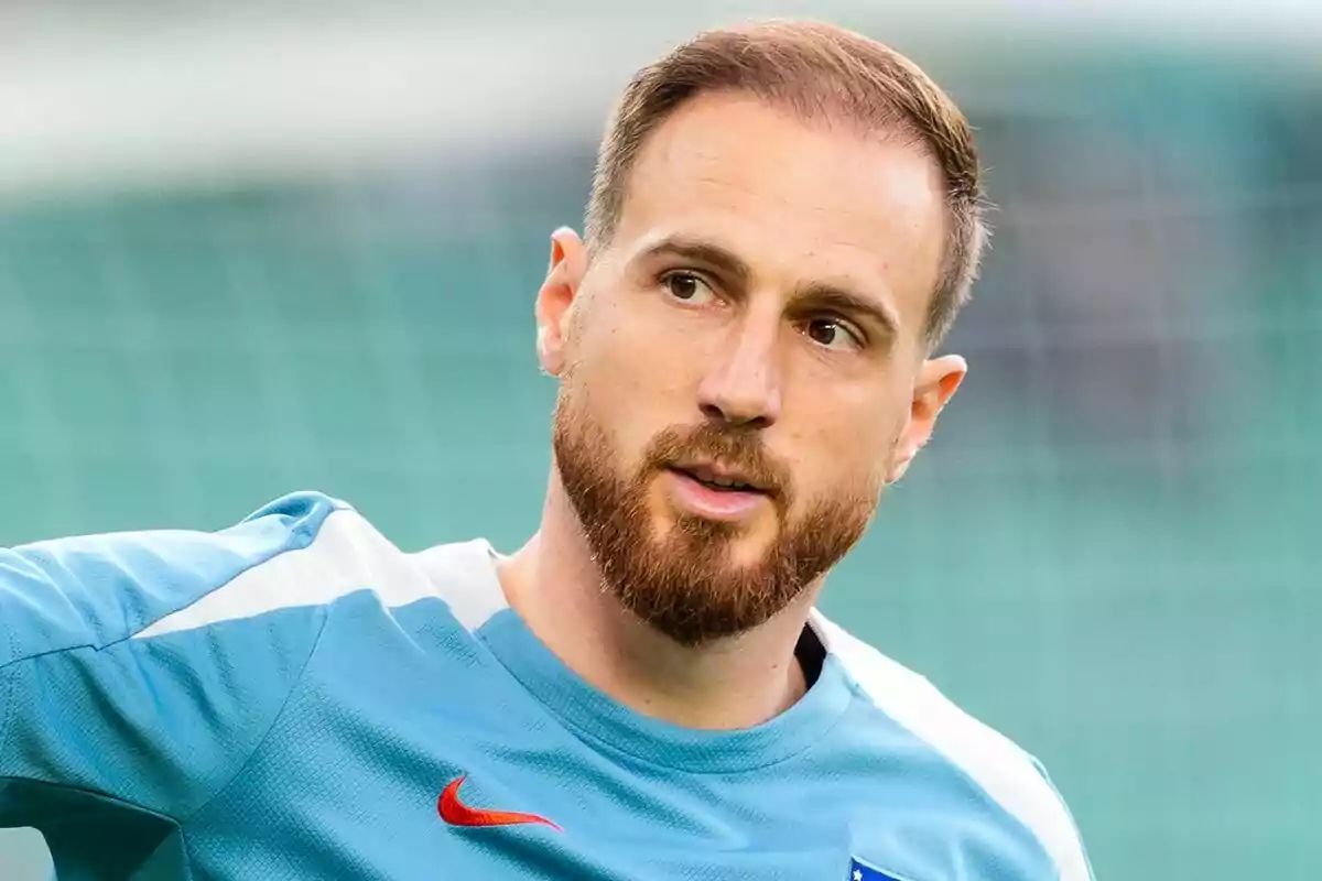 Un hombre con barba y cabello corto lleva una camiseta deportiva azul claro con un logotipo rojo.