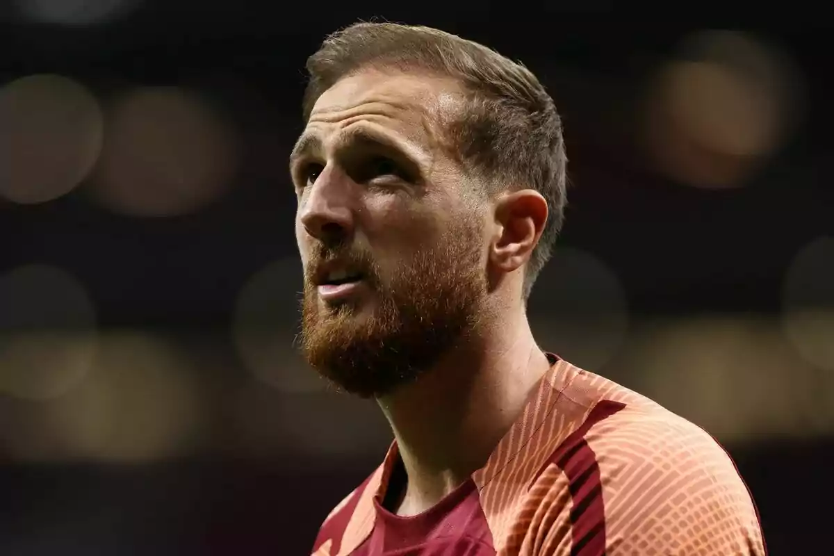 Un hombre con barba y cabello corto, vistiendo una camiseta deportiva, mira hacia arriba con una expresión seria.