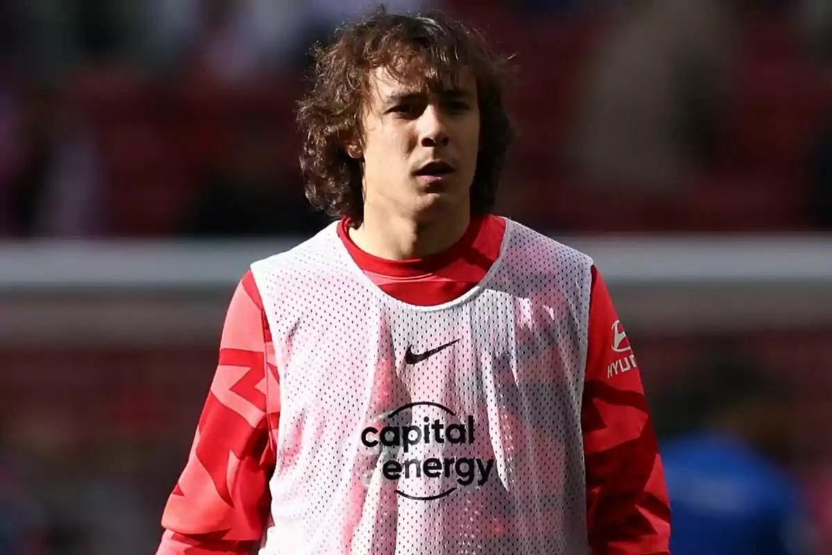 Un jugador de fútbol con chaleco de entrenamiento blanco y camiseta roja en un estadio.