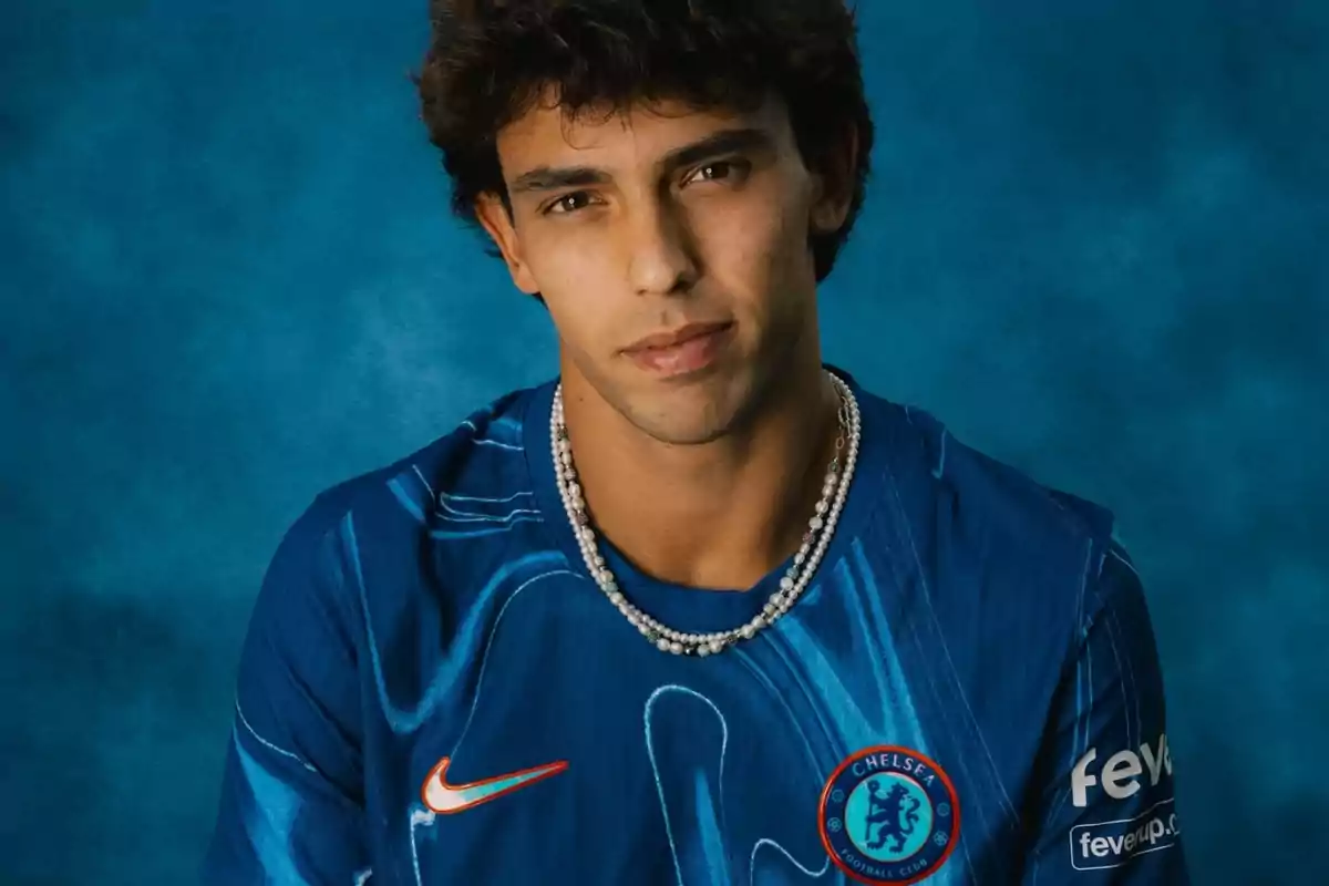 Un hombre con una camiseta azul del Chelsea FC y un collar de perlas, posando frente a un fondo azul.