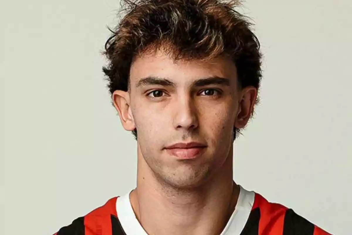 A young man with dark, curly hair is wearing a red and black striped t-jersey.