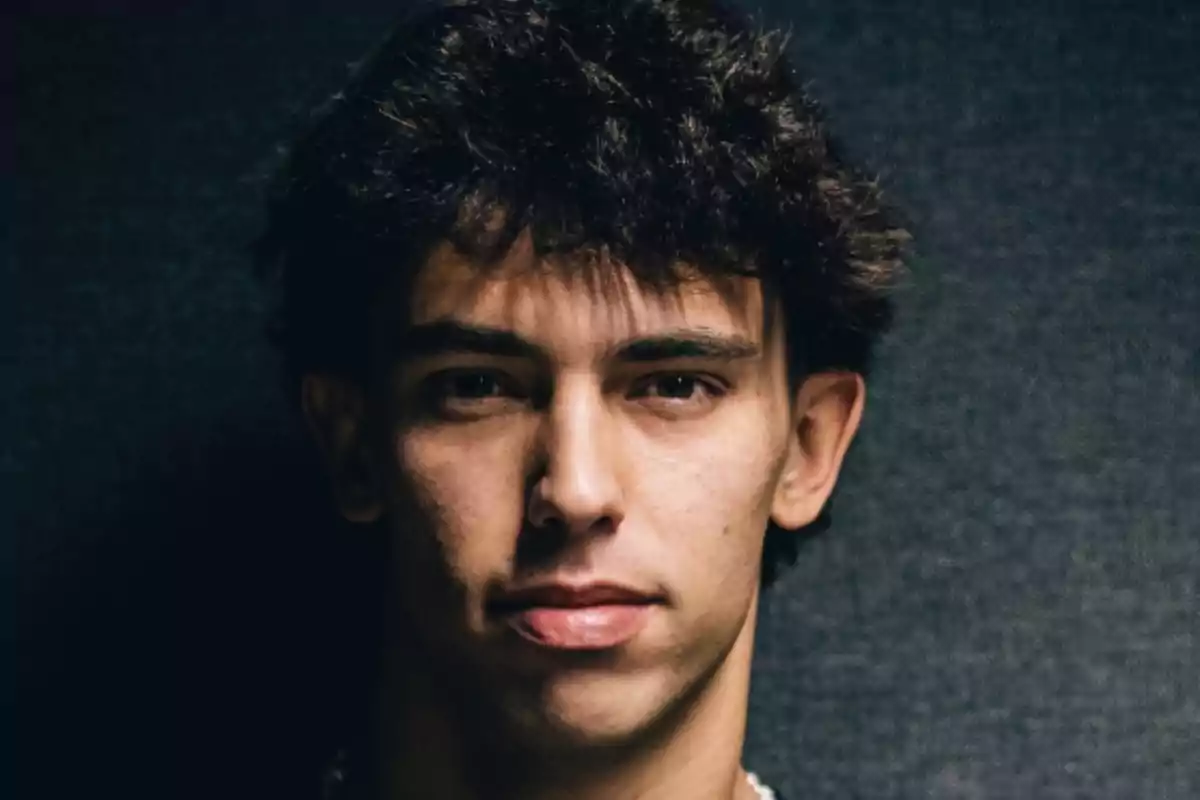 Un hombre joven con cabello oscuro y expresión seria frente a un fondo oscuro.