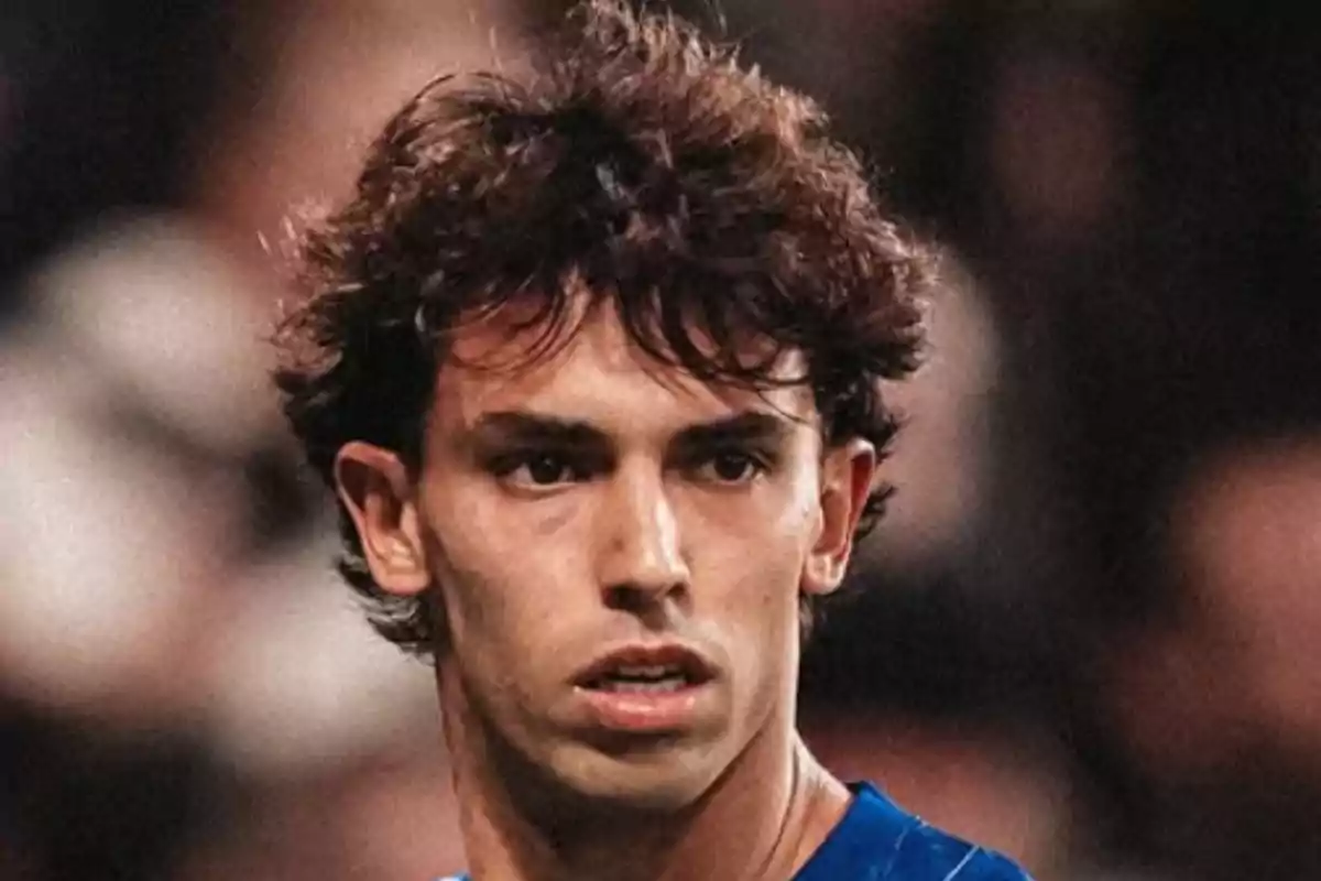 Un hombre con cabello rizado y expresión seria, vistiendo una camiseta azul, en un entorno desenfocado.