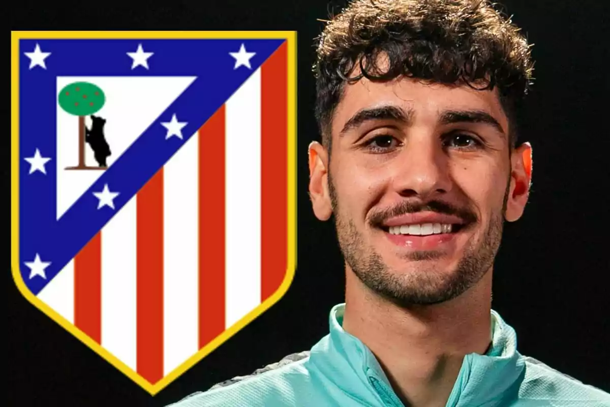 Un joven con barba y cabello rizado sonríe frente al escudo del Atlético de Madrid