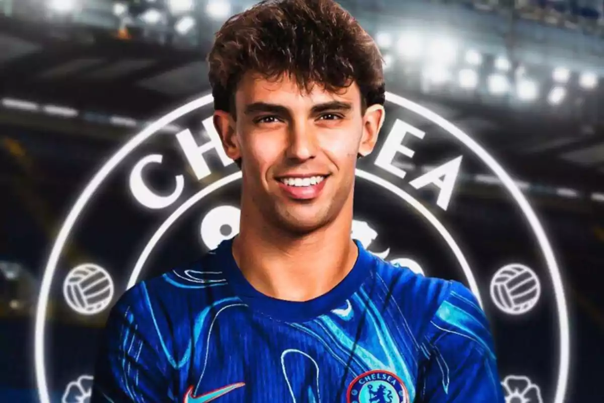 Un jugador de fútbol con la camiseta del Chelsea sonriendo frente al logo del equipo.