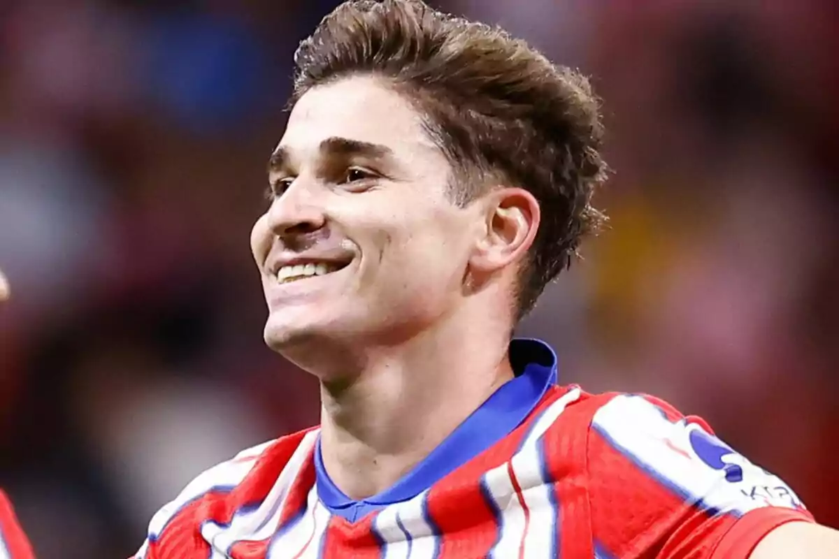 Un jugador de fútbol sonriendo con una camiseta a rayas rojas, blancas y azules.