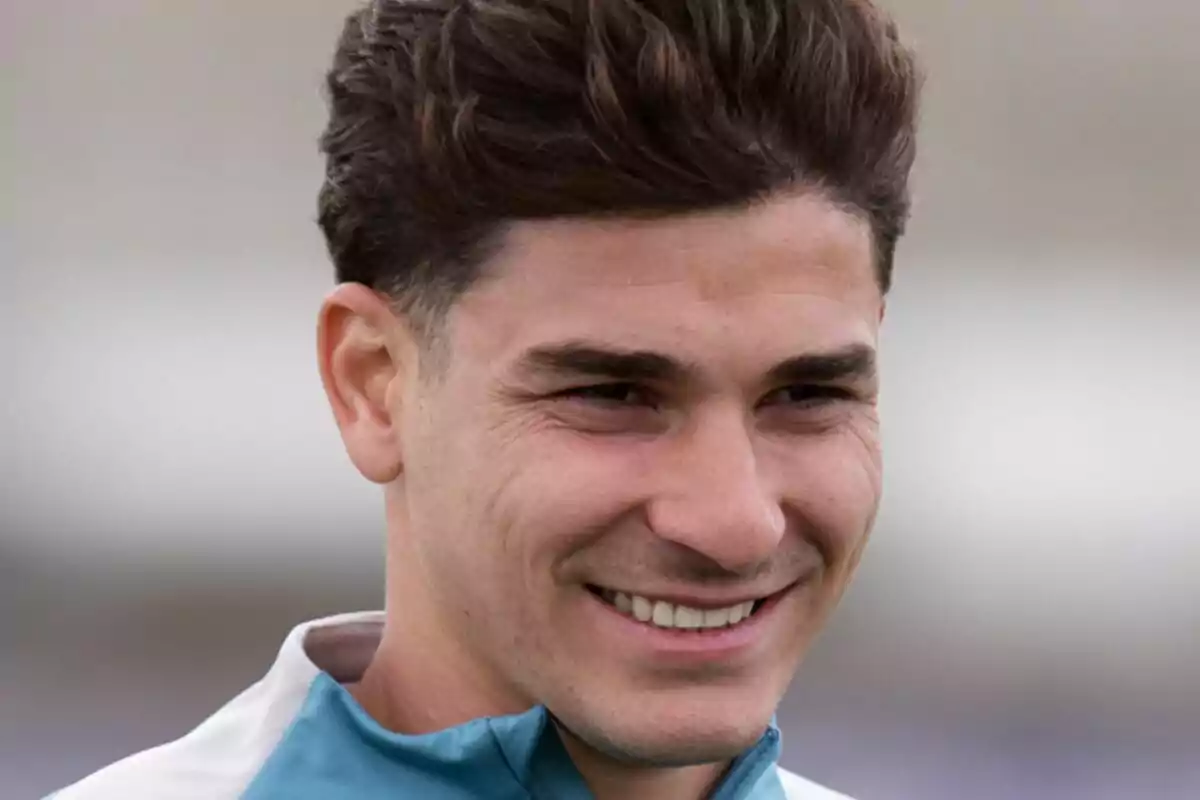 Un hombre joven sonriendo con el cabello oscuro y corto, vistiendo una chaqueta deportiva.