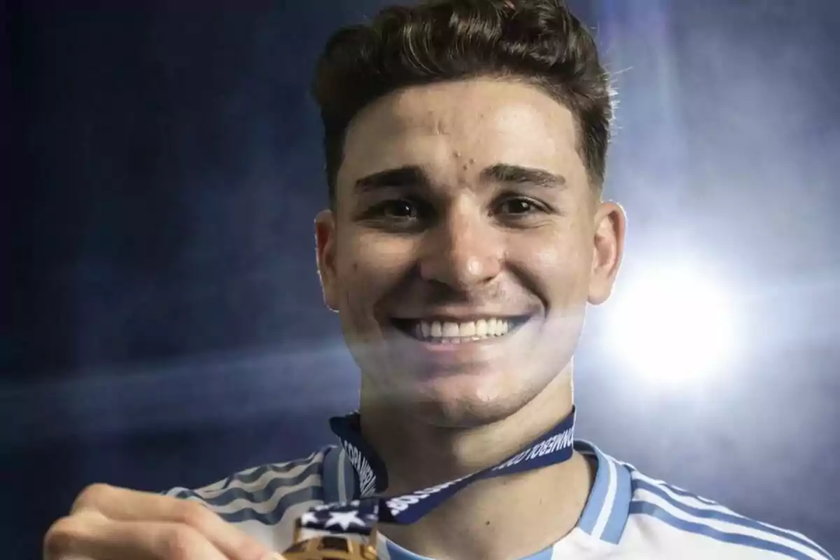 Un hombre sonriente con una medalla de oro alrededor del cuello y una camiseta deportiva a rayas.