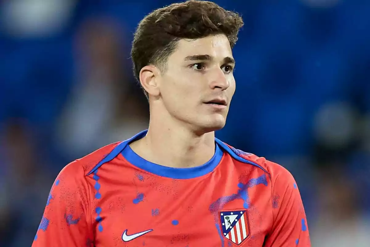 Un jugador de fútbol con camiseta roja y azul del Atlético de Madrid en un estadio.