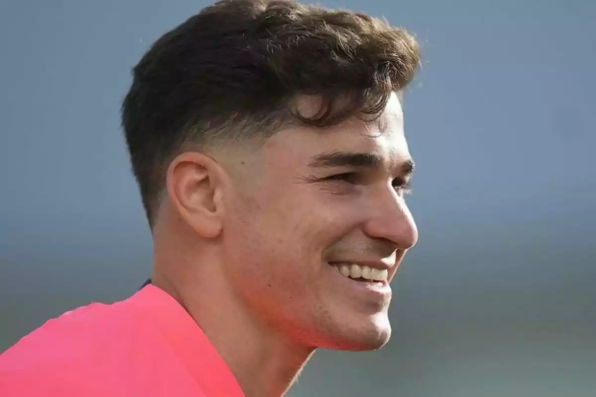 Un hombre joven sonriendo con una camiseta rosa.