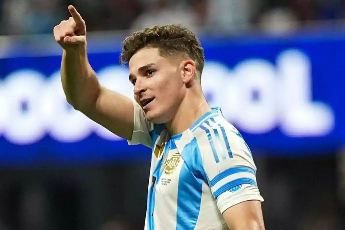 Un jugador de fútbol con la camiseta de Argentina señala con el dedo mientras celebra en el campo.